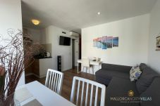 Sala de estar con sofá gris, mesa de comedor blanca, cocina abierta totalmente equipada y decoración náutica en las paredes.