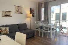 Living-dining room with a gray sofa, white table, chairs, and nautical decorations on the wall.